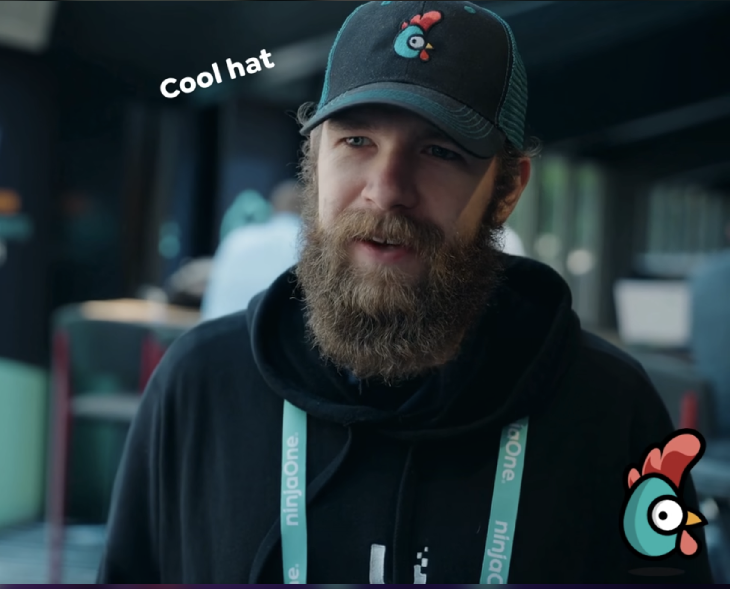 A bearded attendee in a Rewst chicken cap at an event.